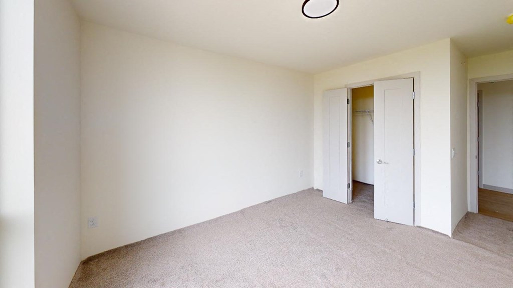 a bedroom with white walls and carpet and a door to a closet