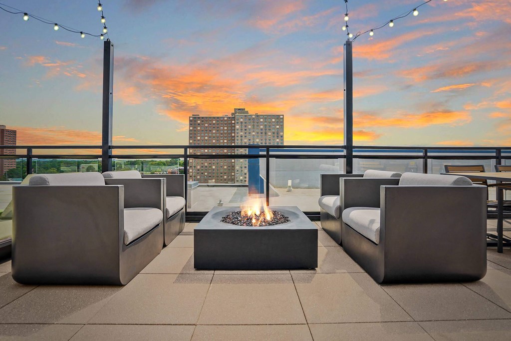 a seating area with a fire pit on a rooftop overlooking a city and a sunset