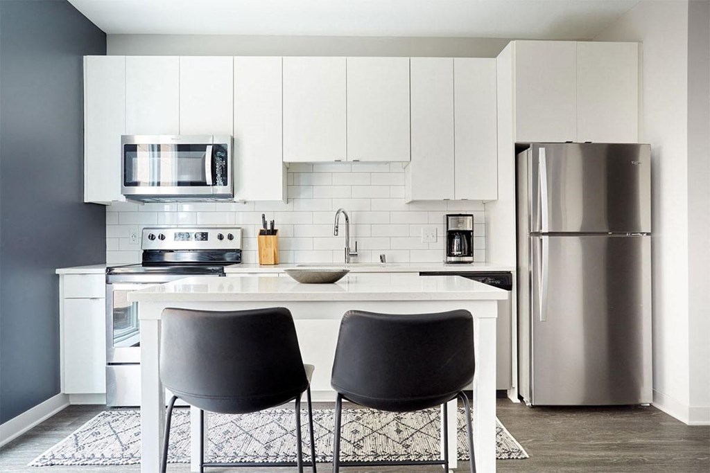 a white kitchen with black chairs and a stainless steel refrigerator