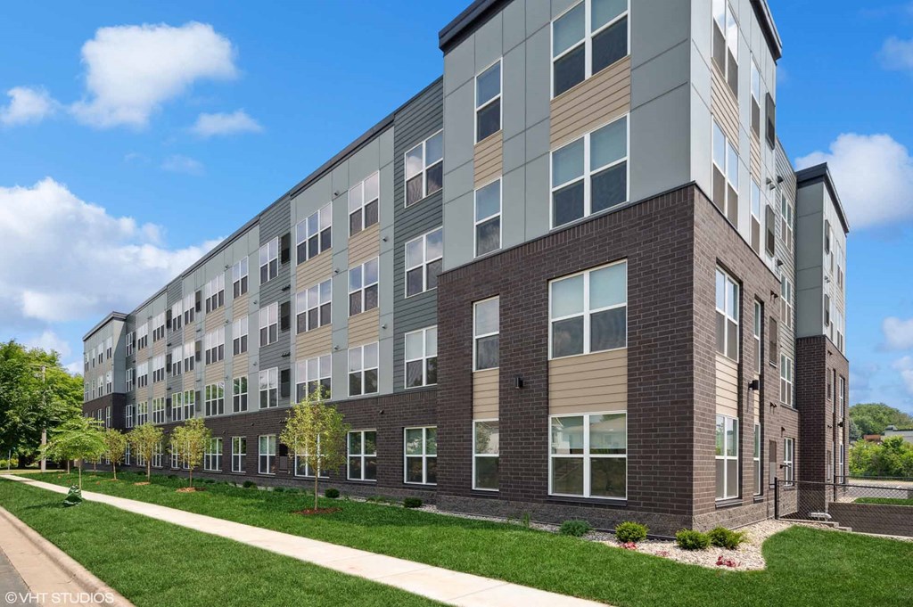 a large brick apartment building with green grass and a sidewalk