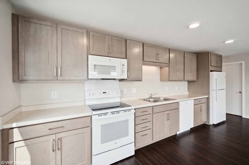 an empty kitchen with white appliances and wooden floors