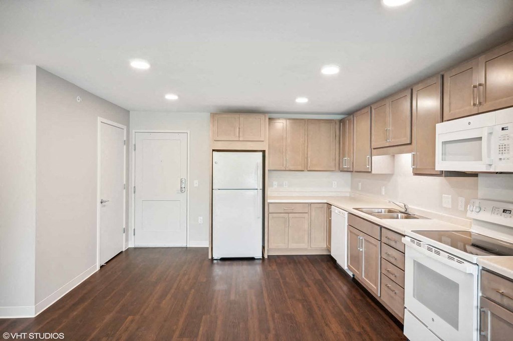 an empty kitchen with white appliances and wooden floors