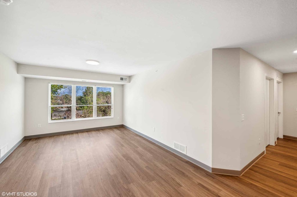 A room with wooden floors and a large window with a view of trees outside.
