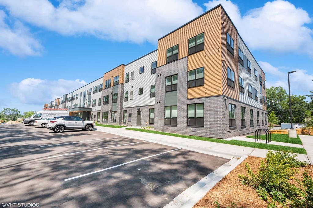 A modern multi-story building with a parking lot in front.
