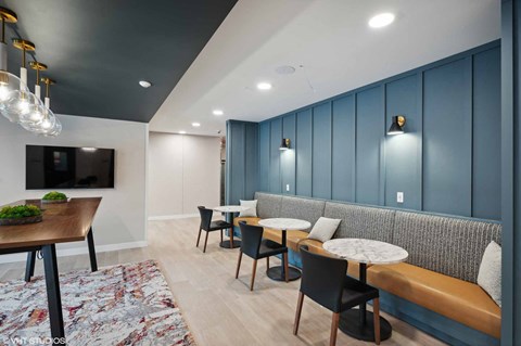 A modern living room with a wooden table and chairs, a sofa, and a TV mounted on the wall.
