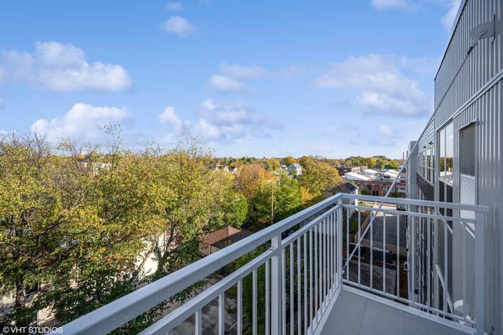 A balcony with a metal railing overlooks a cityscape with buildings and trees.