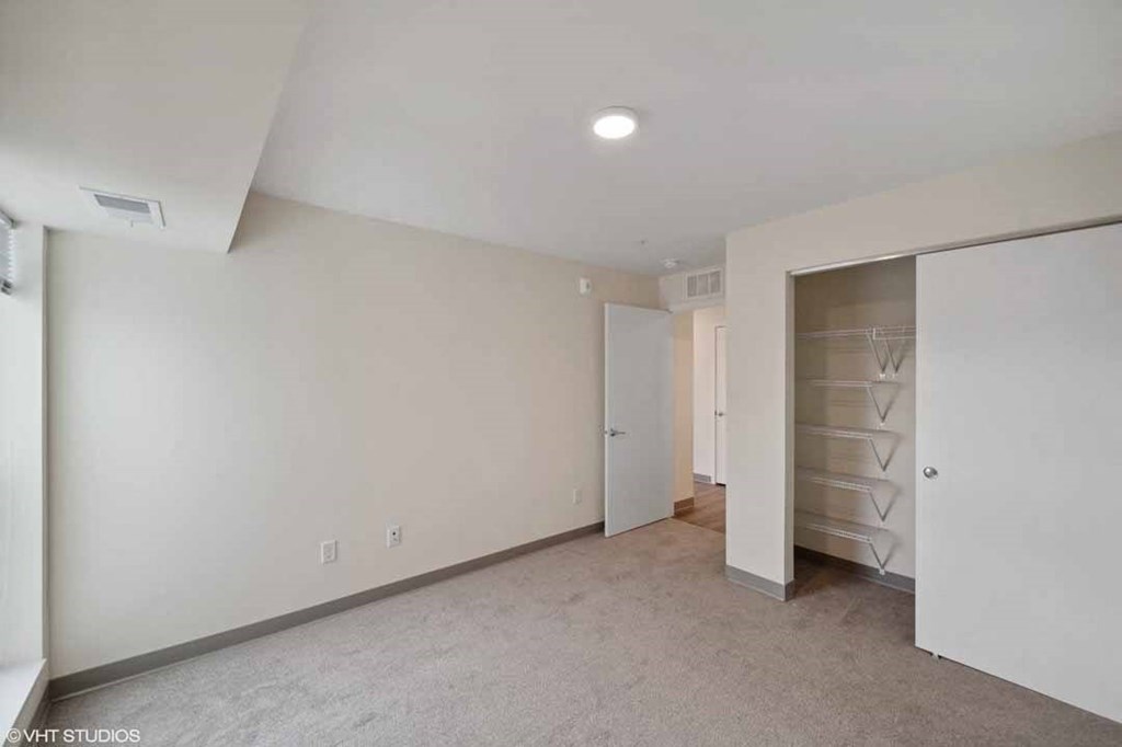 A spacious room with a white door and a white closet with drawers.