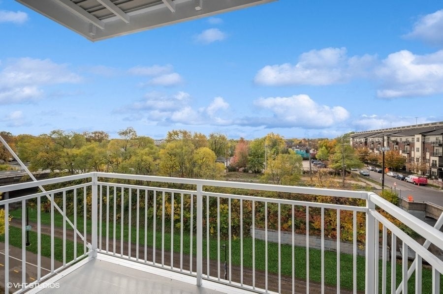 A balcony with a metal railing overlooks a street with cars and buildings.