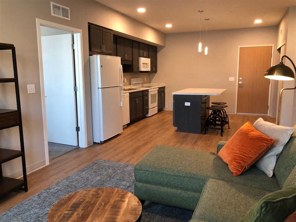 a living room with a couch and a kitchen with a refrigerator