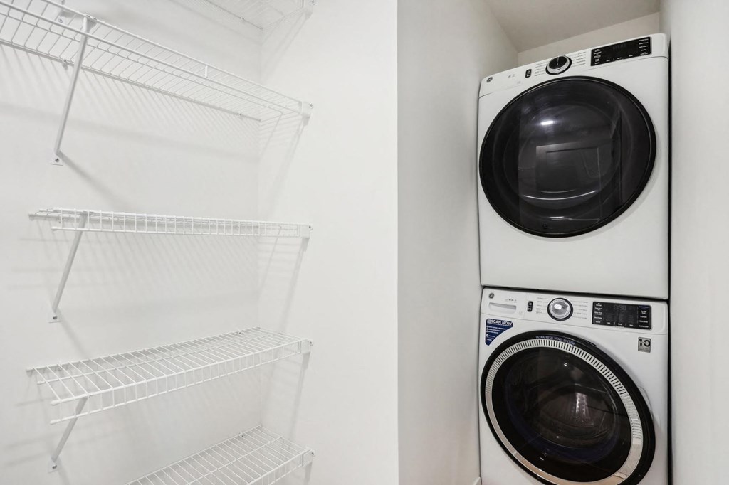 A white dryer is stacked on top of an empty dryer in a white laundry room.