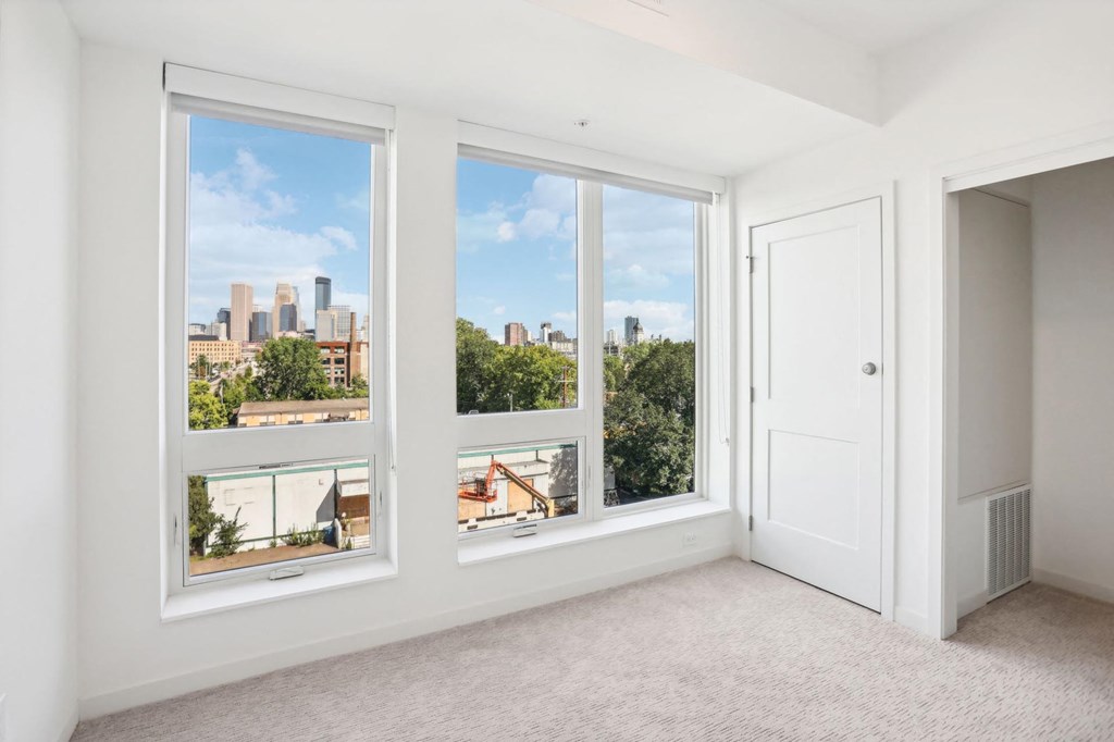 A room with three windows showing a cityscape and greenery outside.
