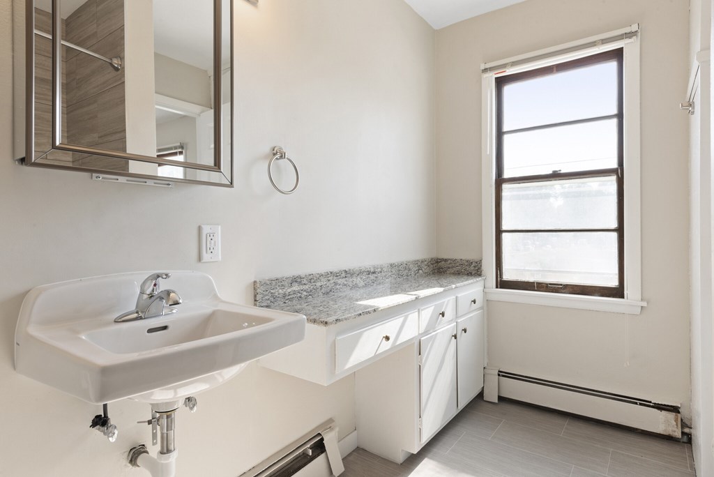 A bathroom with a sink, mirror, and window.