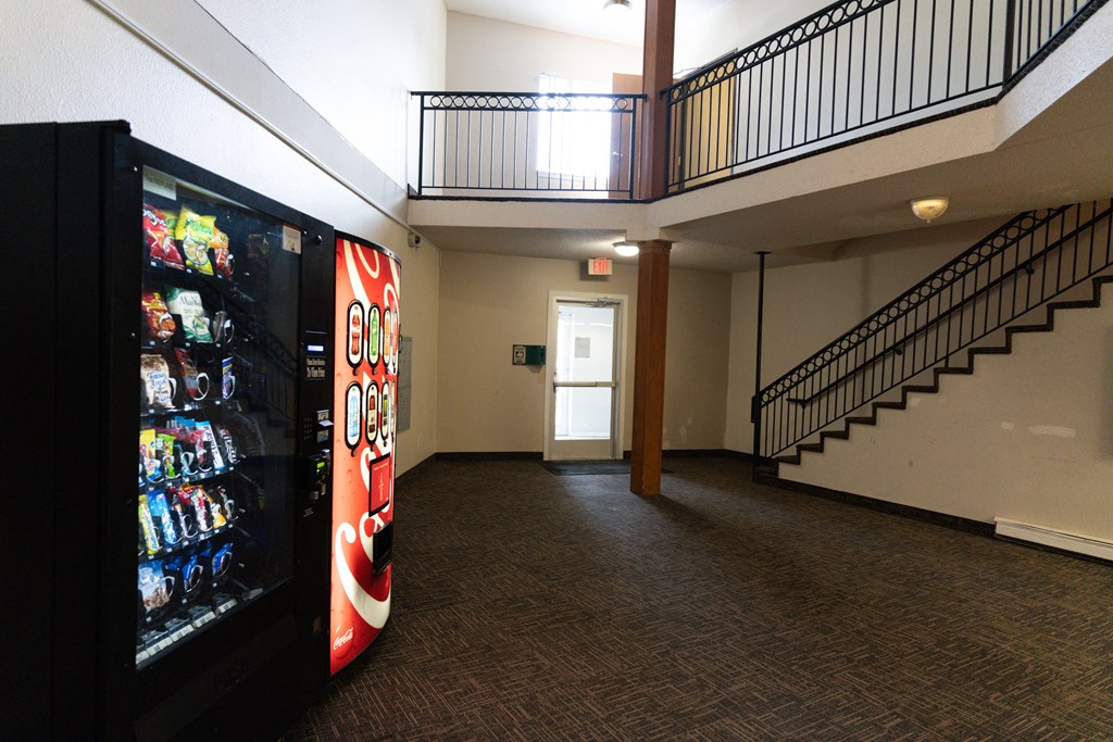 A vending machine is on the left of a hallway with a staircase on the right.