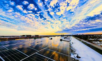 A large solar panel array stretches across the frame under a sky with clouds.
