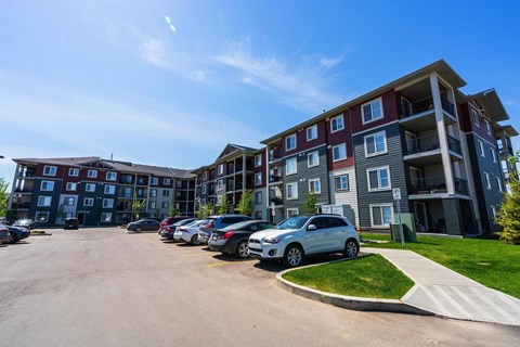 A white car is parked in a parking lot in front of a large apartment building.