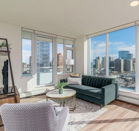 A living room with a green couch and a large window overlooking a cityscape.