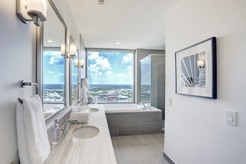 a bathroom with a large window, soaking tub, and double sinks at market square tower in downtown houston