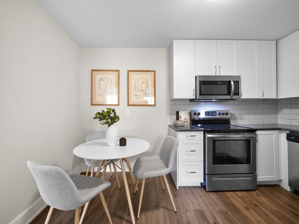 a kitchen with white cabinets and stainless steel appliances and a small white table with three chairs
