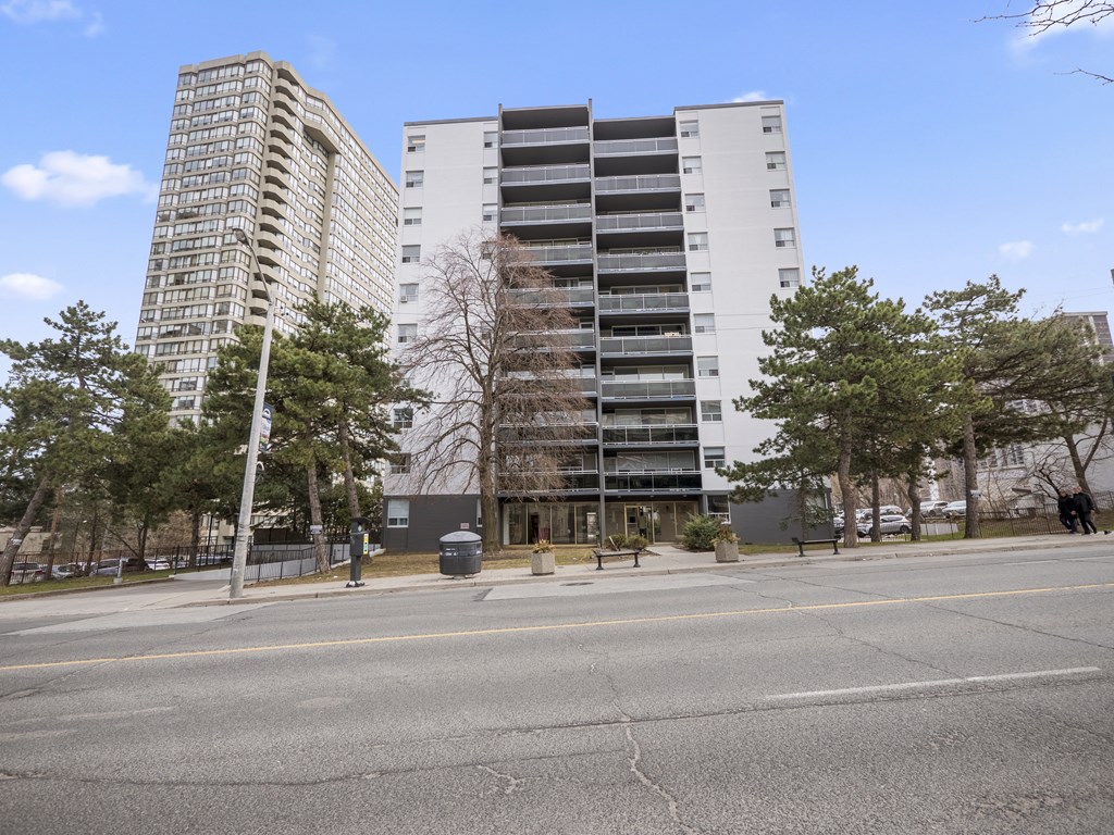 a view from across the street of two buildings with trees in the foreground and a blue sky