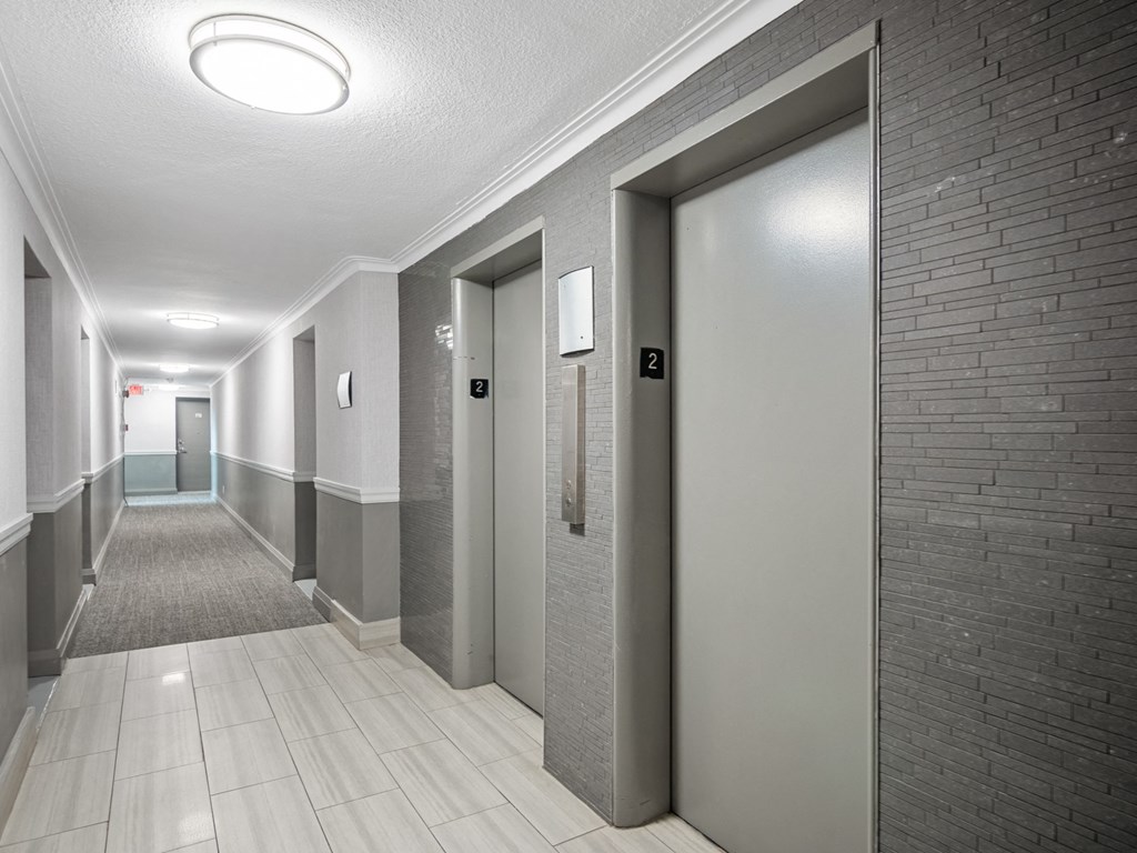 a hallway with three elevators and a brick wall