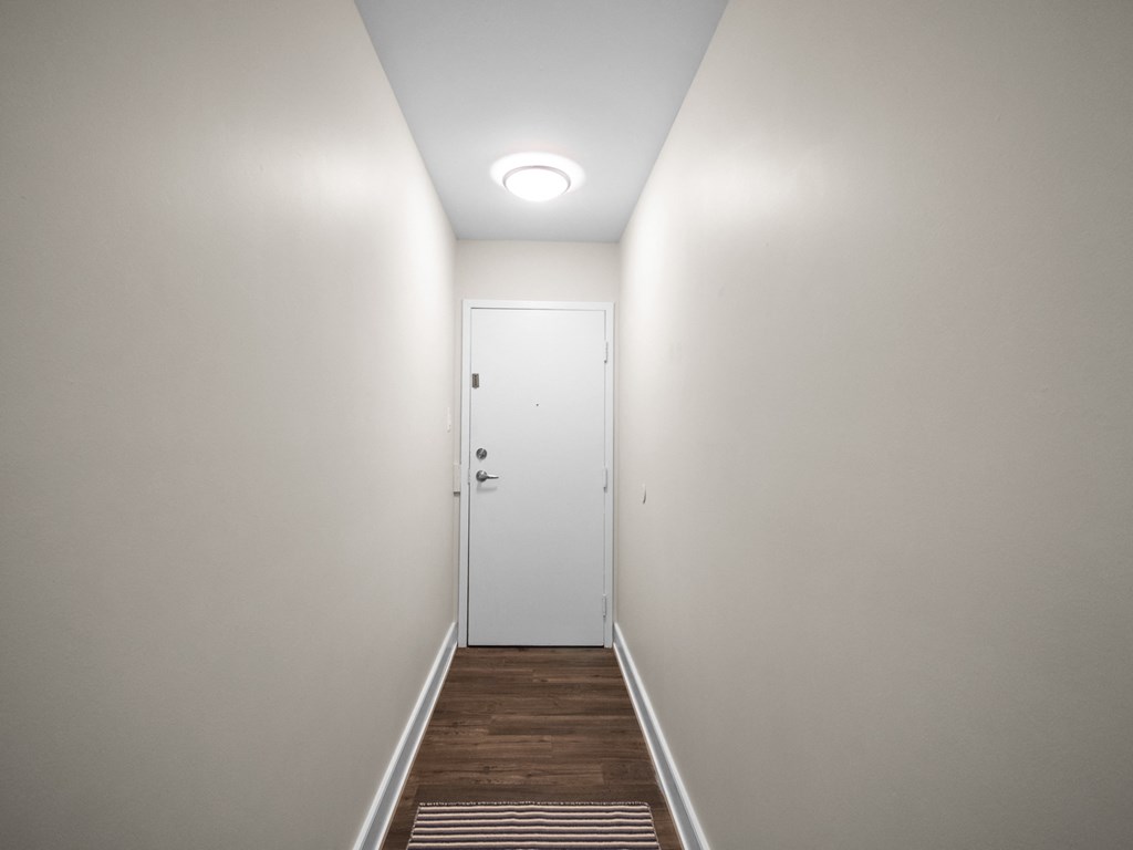 a hallway with white walls and a wooden floor with a white door at the end of it