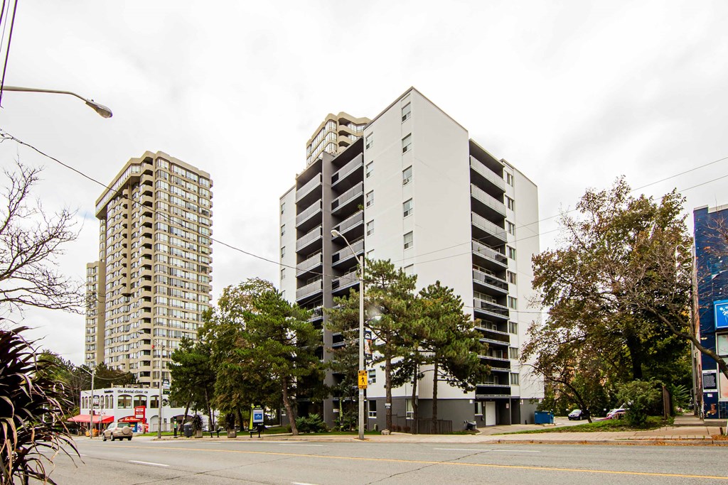 a view from the street of two high rise buildings with balconies and trees in the foreground