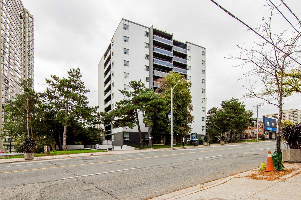 a view from the street of a white apartment building with a blue sign in the background