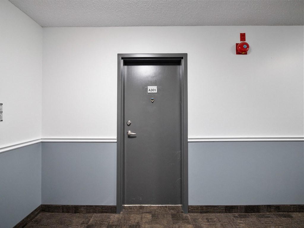 a metal door in a gray walled room with a red fire hydrant above it