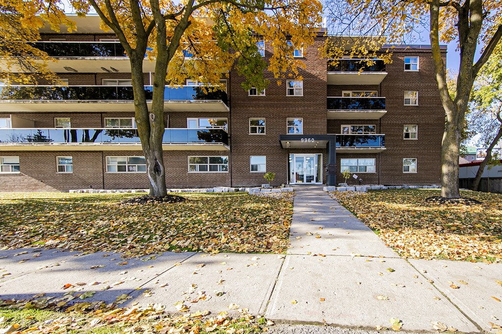 an apartment building with a sidewalk and trees in front of it