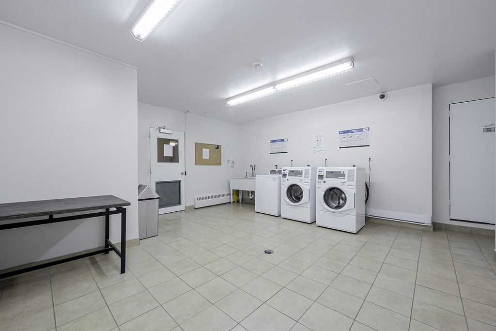 a laundry room with four washing machines and a table with a bench