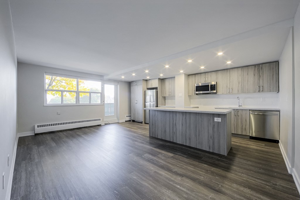 a kitchen and living room in an apartment with hardwood floors and a large window