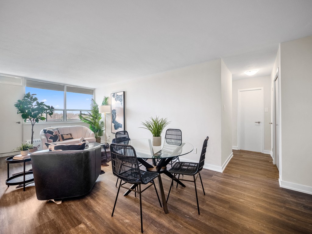 a dining area with a glass table and chairs, a couch and a window with a view