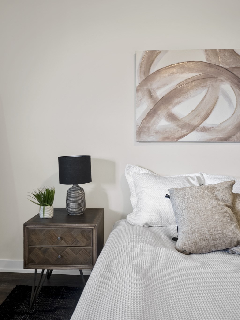a bedroom with white bedding and a brown nightstand with a lamp and a plant