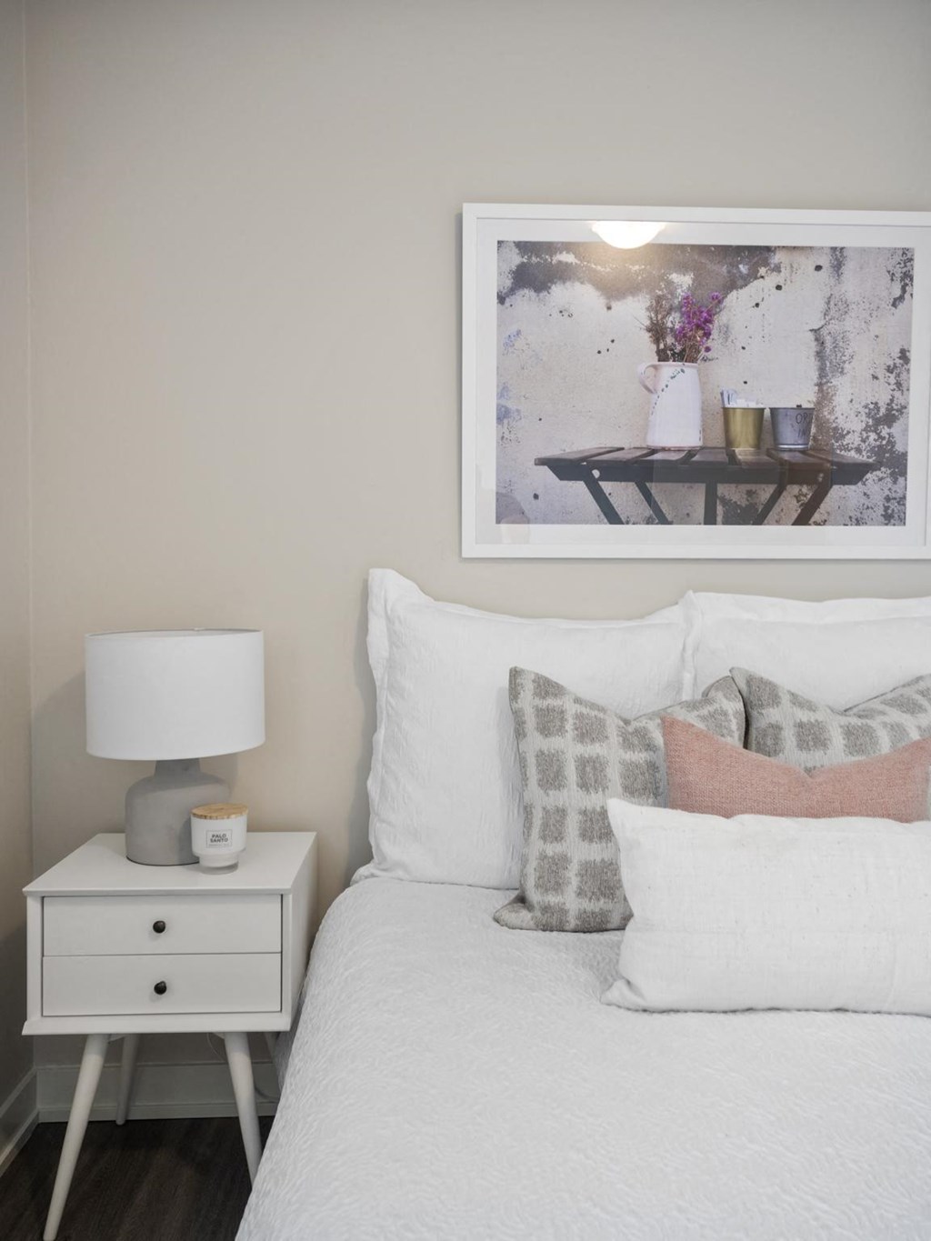 a bedroom with white bedding and a white nightstand with a lamp on it