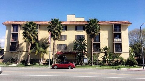 a red car parked in front of a building with palm trees