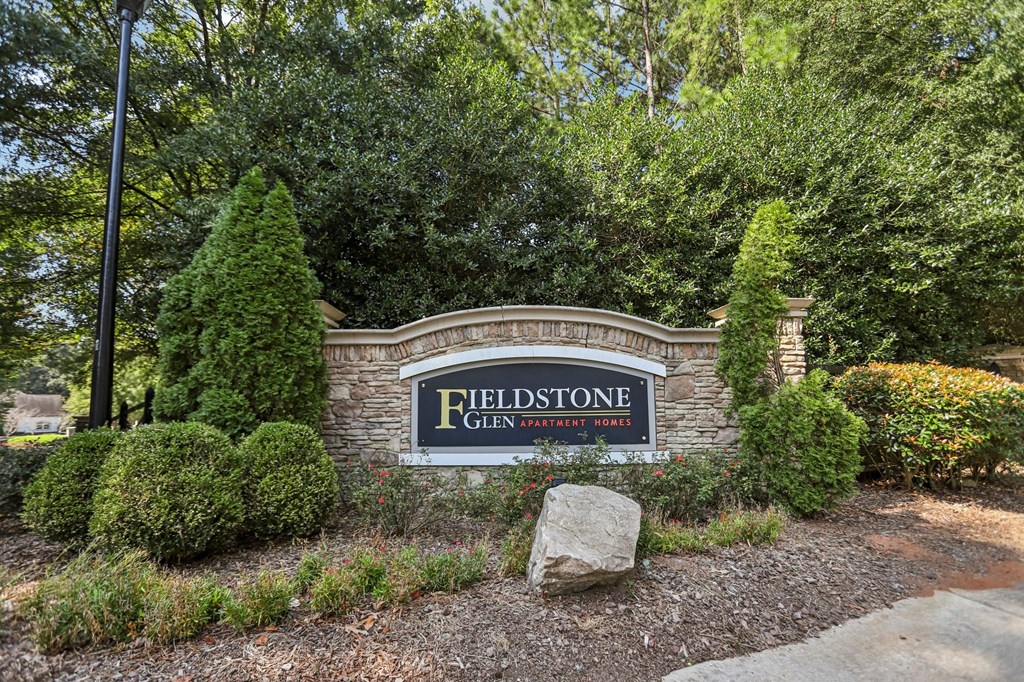 A sign that says Fieldstone in front of a green hedge.