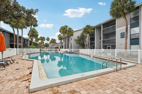 A swimming pool surrounded by a white fence and palm trees.