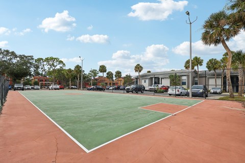 A tennis court with a red and green surface is surrounded by trees and buildings.