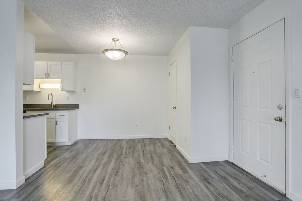 an empty living room and kitchen with white walls and wood flooring