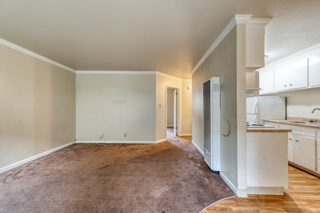 an empty living room with a kitchen in the background