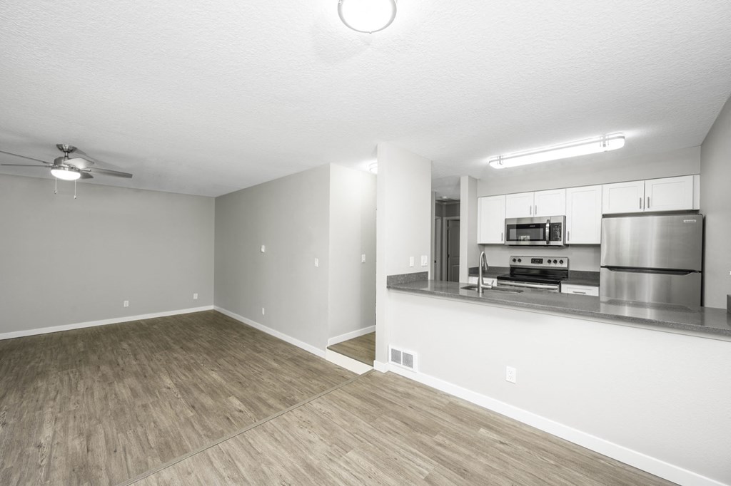 an empty living room with a kitchen in the background