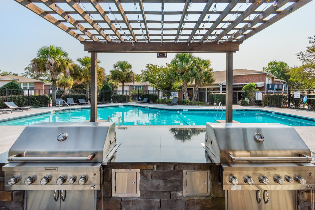 two gas bbq grills with a pool in the background