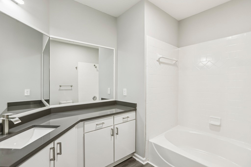 A white bathroom with a sink, mirror, and bathtub.