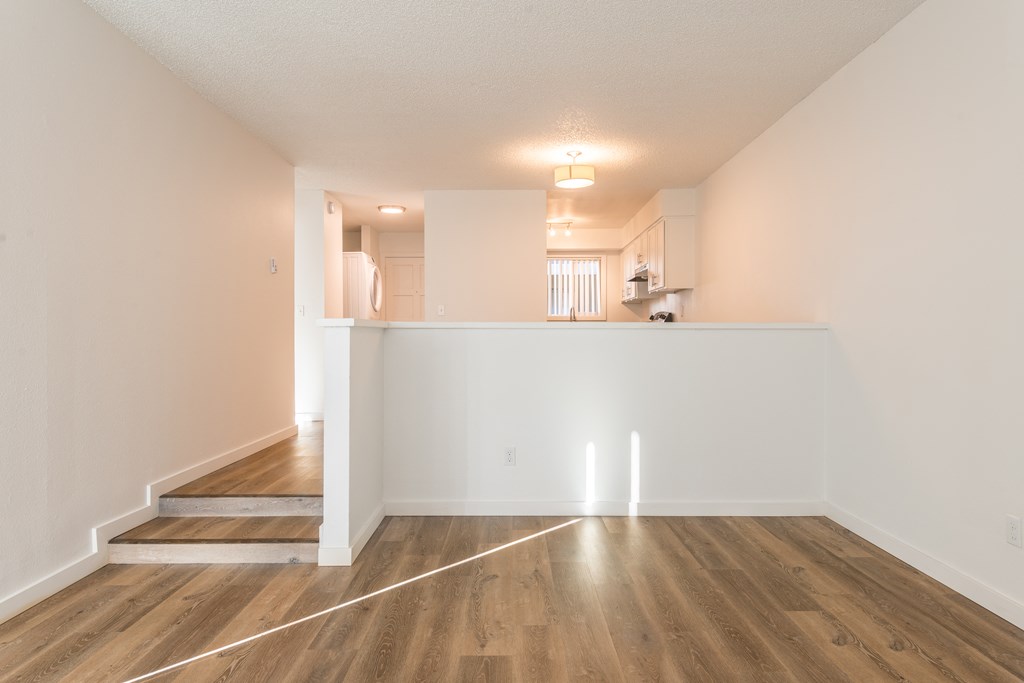 a living room and dining room with hardwood floors and a kitchen in the background