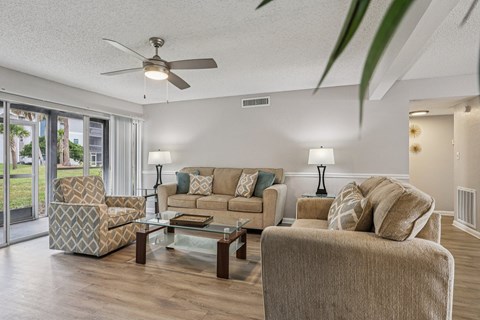 A living room with a beige couch, a glass coffee table, and a ceiling fan.