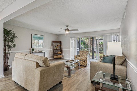 A living room with a beige couch, a glass coffee table, and a ceiling fan.