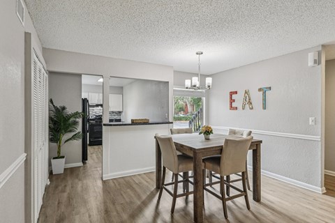 A dining room with a table and chairs and a kitchen in the background.