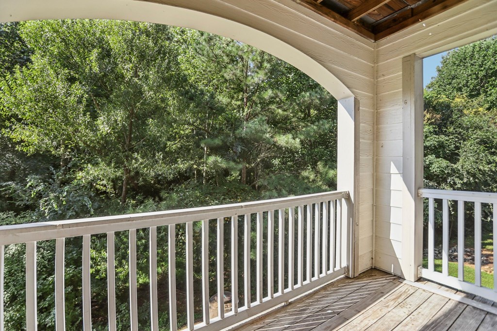 A balcony with a white railing and a view of a wooded area.