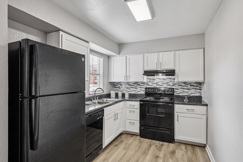 A black refrigerator stands in a kitchen with white cabinets and black appliances.