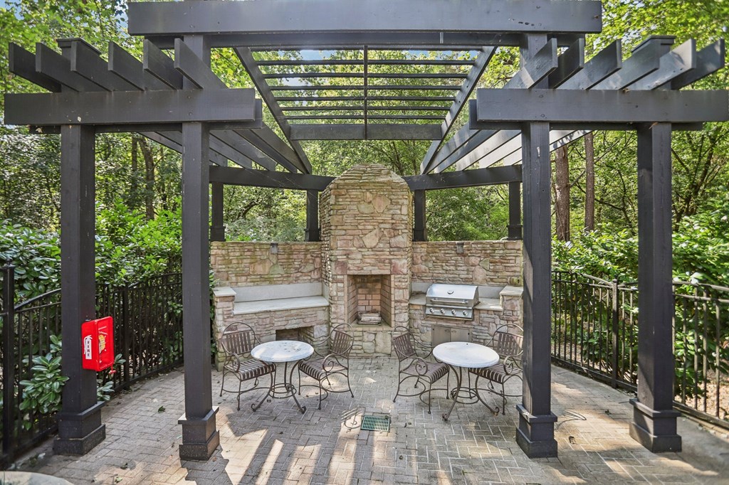 A patio with a fireplace and chairs under a pergola.